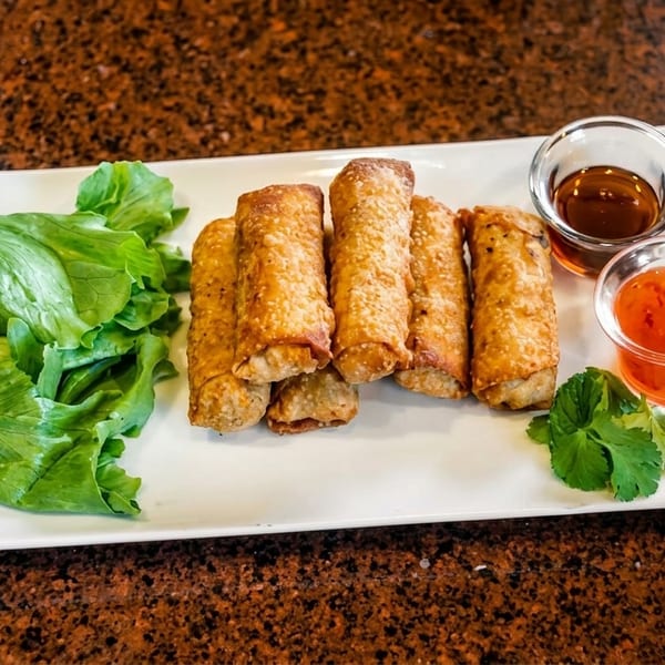 Crispy golden egg rolls, fresh lettuce, cilantro, and two dipping sauces on a white rectangular plate.