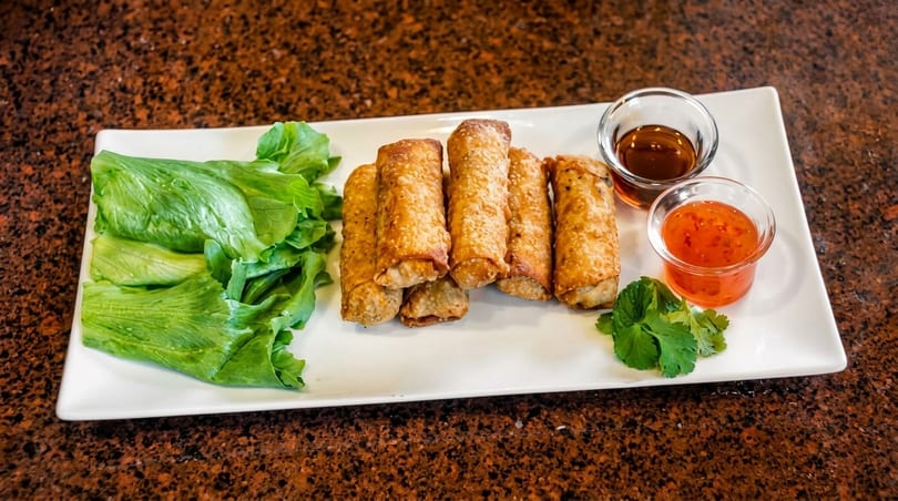 Crispy golden egg rolls, fresh lettuce, cilantro, and two dipping sauces on a white rectangular plate.